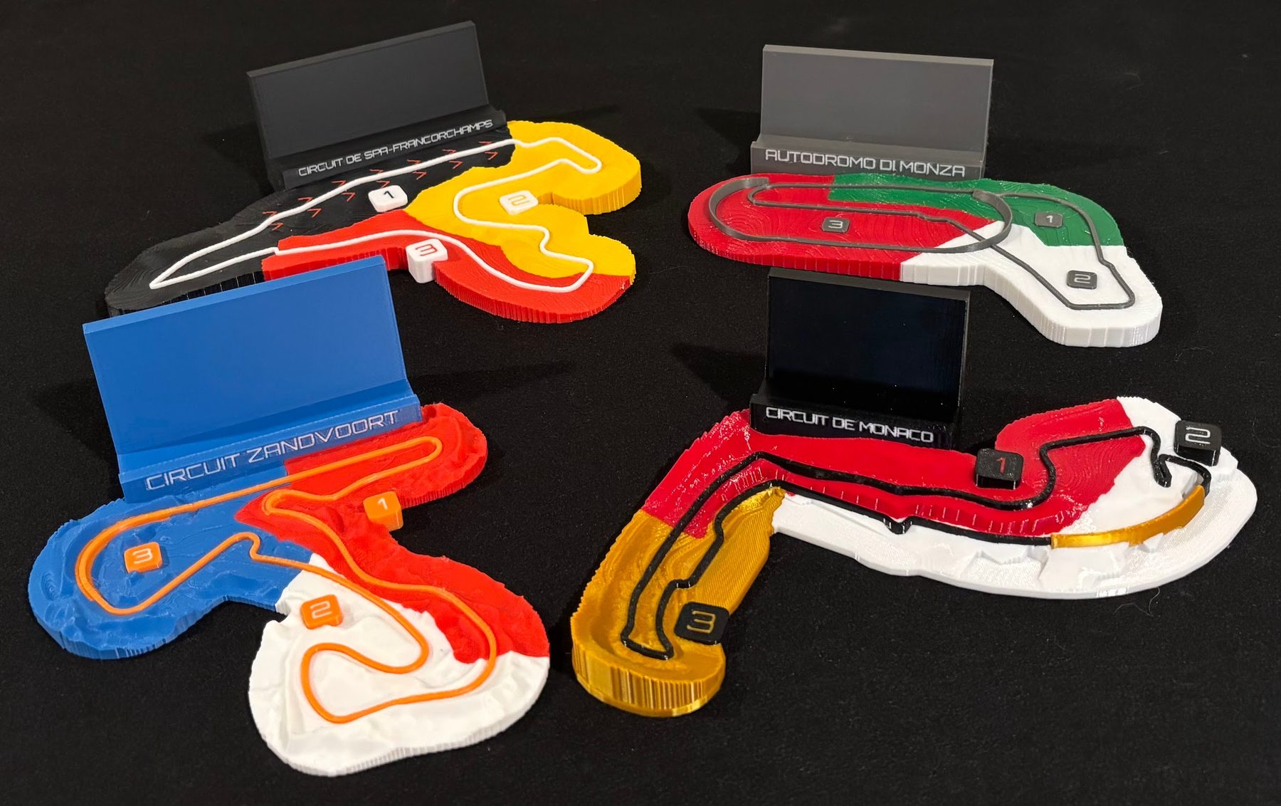 Monaco, Spa, Zandvoort, Monza relief maps with their nameplate stands, on a black mat