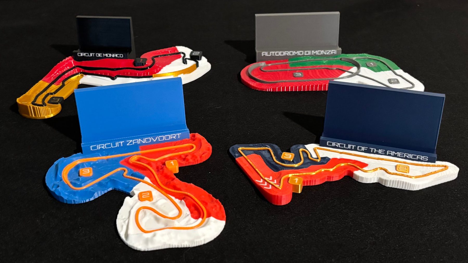 Monaco, Monza, Zandvoort, Circuit of the Americas relief maps with their nameplate stands, on a black mat